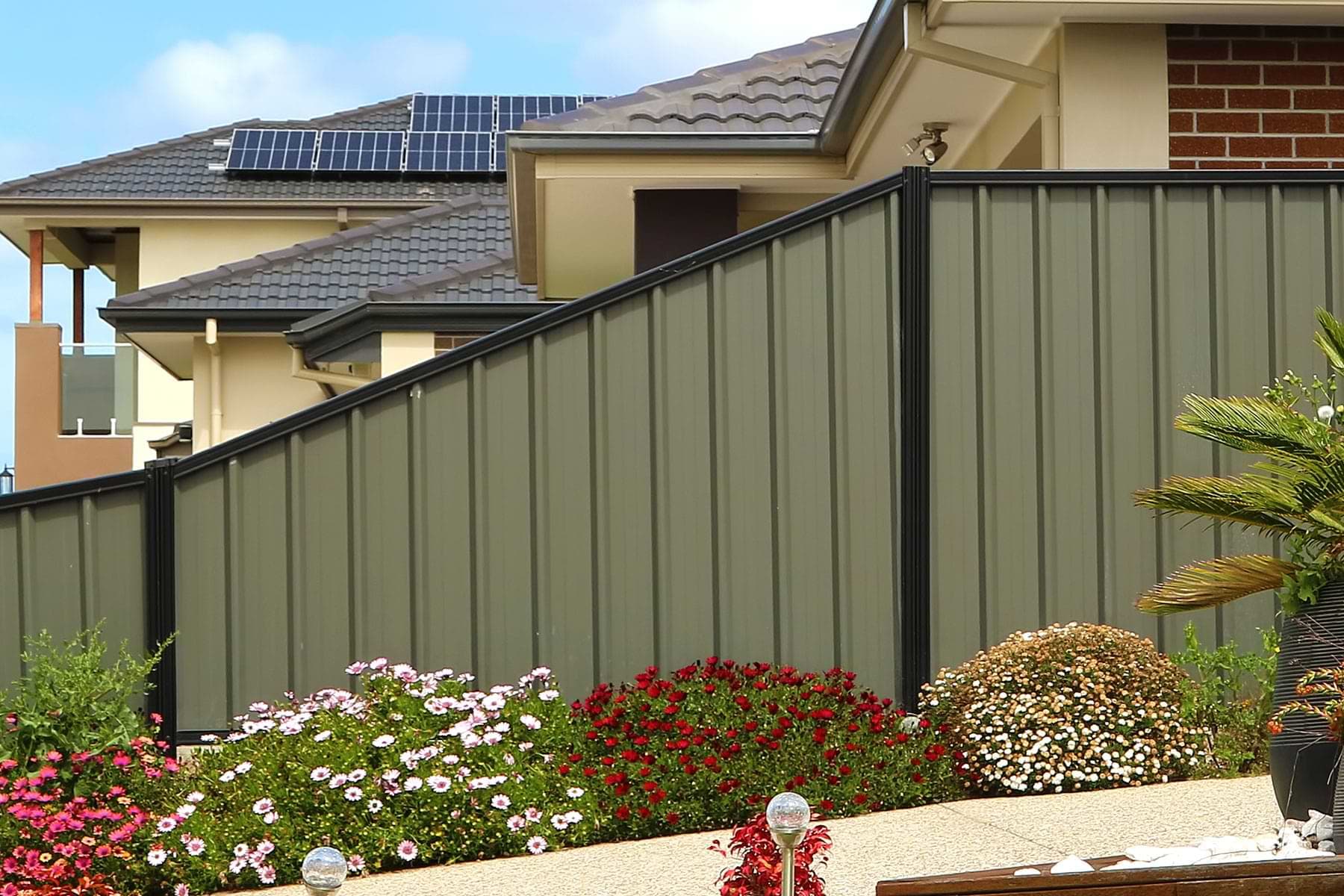 Installed steel privacy fence with dark posts and landscaped planting bed.