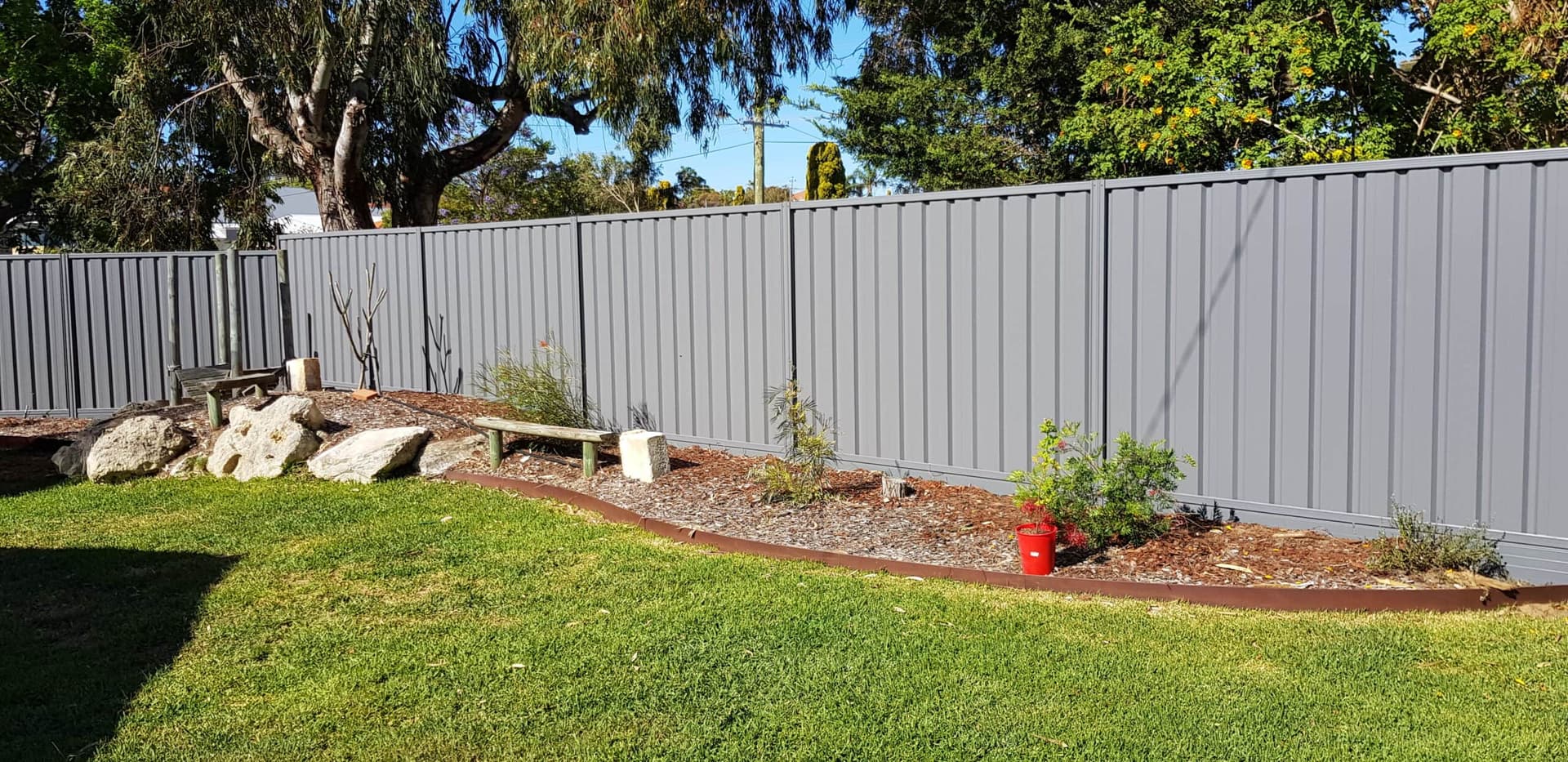 Installed gray steel privacy fence along a landscaped backyard boundary.