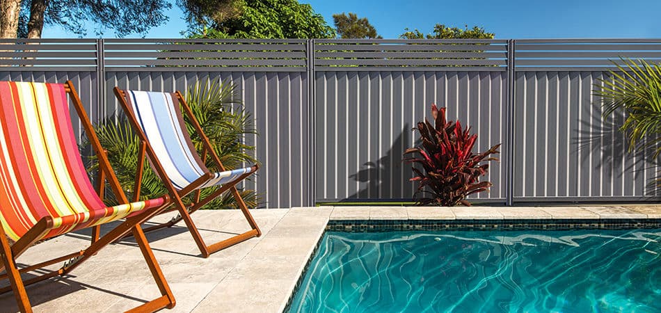 Installed charcoal steel privacy fence around a pool area with landscaping.